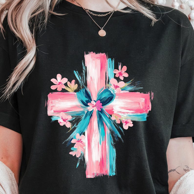 Puede incluir: Una camiseta negra con un dise&ntilde;o de cruz rosa y azul. La cruz est&aacute; rodeada de flores rosas y un lazo azul.