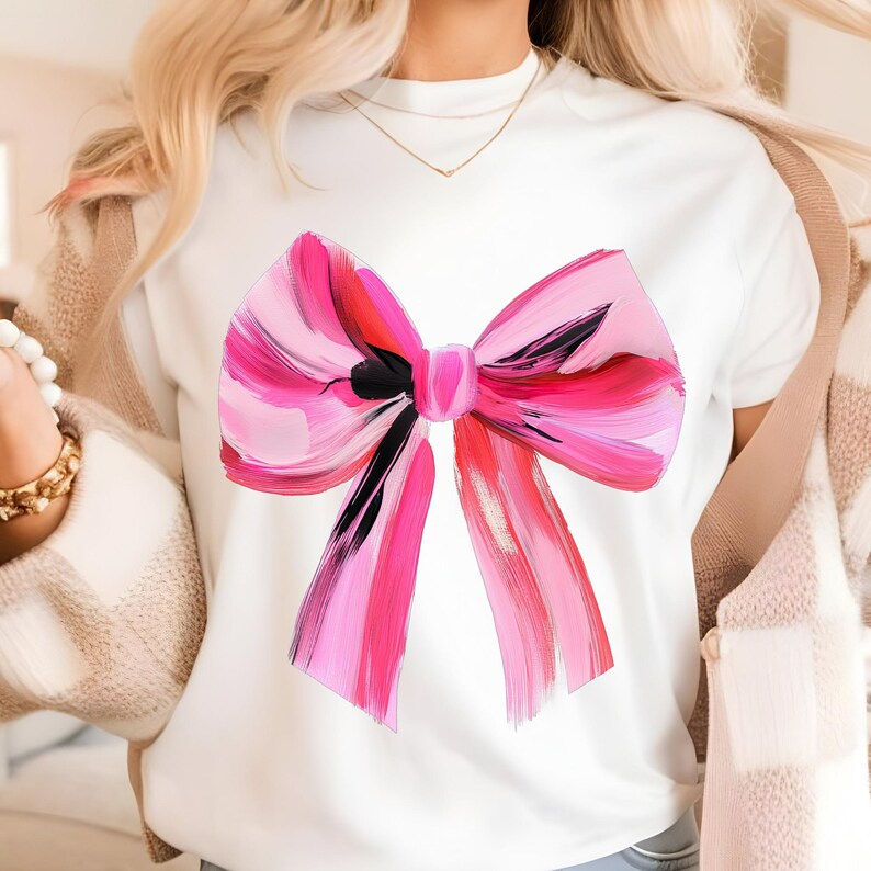 Puede incluir: Camiseta blanca con un dise&ntilde;o de lazo pintado en rosa y rojo.