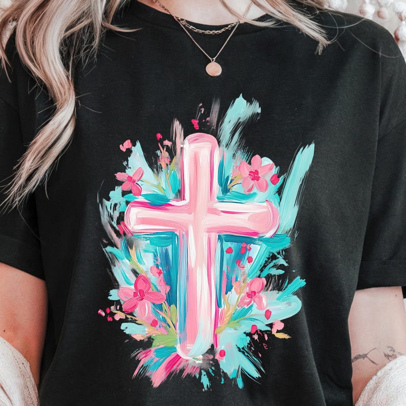 May include: A black t-shirt featuring a pink cross surrounded by blue and pink flowers. The cross is painted in a brushstroke style.