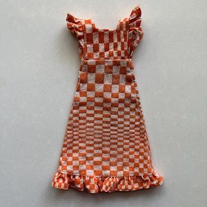 Könnte beinhalten: Orange-weiß kariertes Kleid mit Rüschenärmeln und Saum. Das Kleid hat einen quadratischen Ausschnitt und eine taillierte Taille. Der Stoff scheint ein strukturierter Strick zu sein. Das Kleid ist eine Mini-Länge.