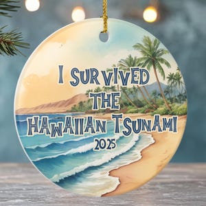 May include: Round ceramic Christmas ornament with a beach scene and the text "I Survived The Hawaiian Tsunami 2025". The ornament has a gold string for hanging and features a tropical landscape with palm trees and ocean waves.