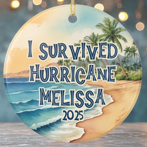 May include: Round ceramic ornament with a beach scene and the text "I Survived Hurricane Melissa 2025." The design features a sandy beach, ocean waves, palm trees, and a sunset sky. A gold string is attached for hanging.