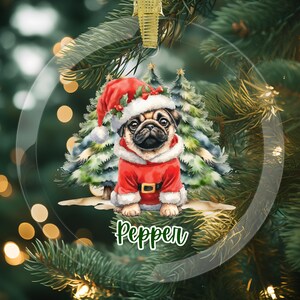 May include: A clear, round Christmas ornament featuring a pug dressed in a Santa Claus outfit. The pug is wearing a red suit and hat with white trim. The ornament has a gold ribbon for hanging and the name "Pepper" in green.