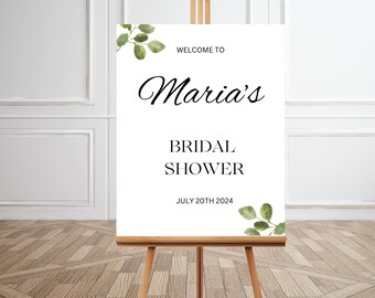 May include: A white sign on a wooden easel, announcing "Maria's Bridal Shower" with the date July 20th, 2024. The sign is decorated with green watercolor eucalyptus leaves.