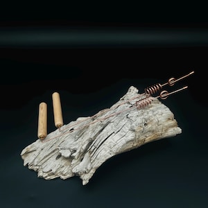 May include: Two copper dowsing rods featuring cylindrical wooden handles. Each rod consists of a long, thin copper wire bent at a right angle, with a coiled section near the tip and a small circular loop positioned just before the end of the wire.