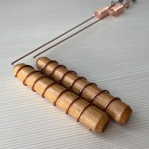 May include: Two cylindrical light brown wooden handles wrapped in thin copper wire. Each handle is attached to a long, thin copper wire frame that extends outward, featuring a small coiled copper spring detail at the end of each wire.