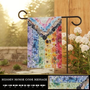 May include: A colorful garden flag with a floral and butterfly design in a rainbow pattern. The flag is displayed on a black metal stand. The text "HIDDEN MORSE CODE MESSAGE" is at the bottom, with a Morse code message.