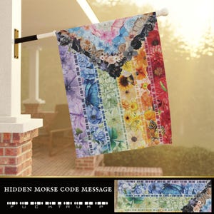 Könnte beinhalten: Eine farbenfrohe Gartenflagge mit Blumen- und Schmetterlingsdesign. Die Flagge zeigt einen Regenbogen aus Farben, mit Blumen und Schmetterlingen in jedem Streifen. Die Flagge hängt an einer weißen Stange. Der Text "HIDDEN MORSE CODE MESSAGE" befindet sich unten.