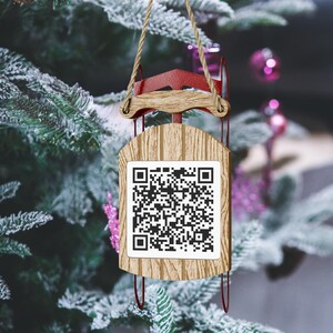 May include: A wooden Christmas bauble shaped like a sledge with a red top and a white QR code on the front.