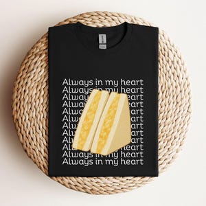 Black t-shirt with yellow tamago sando (Japanese egg sandwich) design and Japanese writing, flat lay style on rattan background