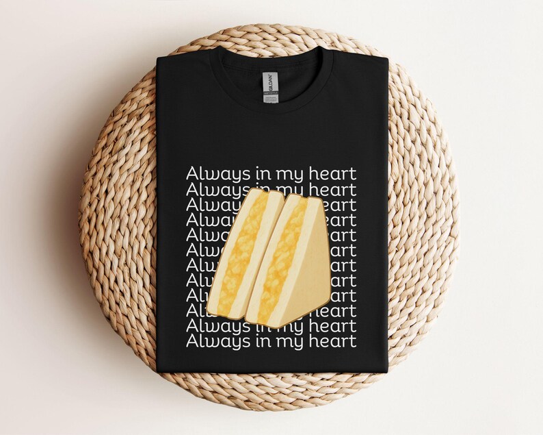 Black t-shirt with yellow tamago sando (Japanese egg sandwich) design and Japanese writing, flat lay style on rattan background
