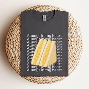 Charcoal t-shirt with kawaii tamago sando (egg sandwich) print and Japanese lettering, flat folded on wicker mat