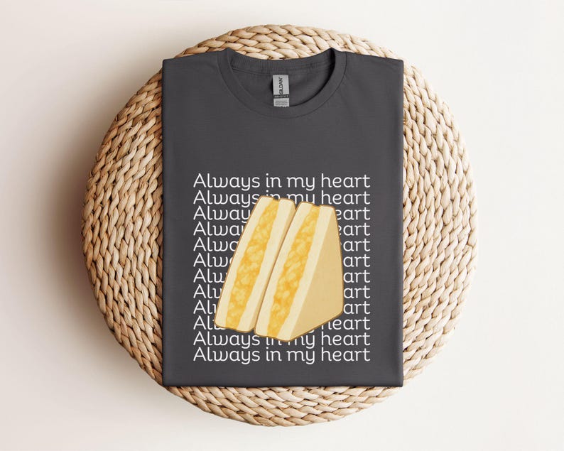 Charcoal t-shirt with kawaii tamago sando (egg sandwich) print and Japanese lettering, flat folded on wicker mat