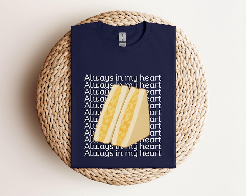 Navy t-shirt with Japanese tamago sando sandwich design and Japanese writing, flat folded on straw background