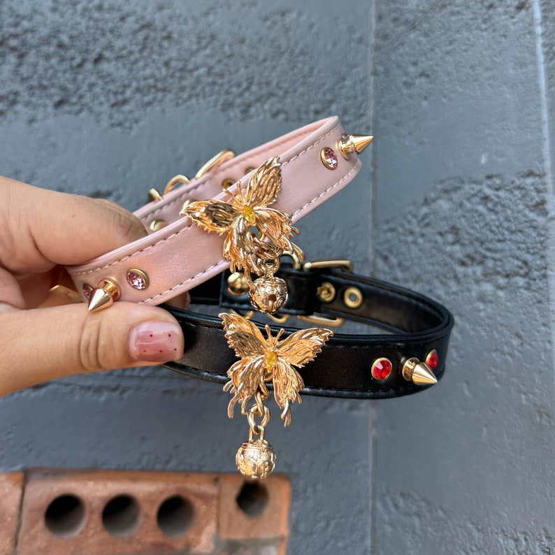 May include: Two leather collars with gold butterfly charms and jeweled accents. The pink collar has pink rhinestones and the black collar has red rhinestones.
