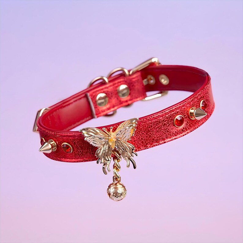 May include: A red leather choker with gold studs and a dangling gold butterfly charm. The butterfly has a yellow center and is attached to a small gold bell.