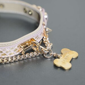 Puede incluir: Un collar de perro de cuero rosa con tachuelas doradas y una cadena dorada unida a una etiqueta dorada en forma de hueso que dice "Poppy".