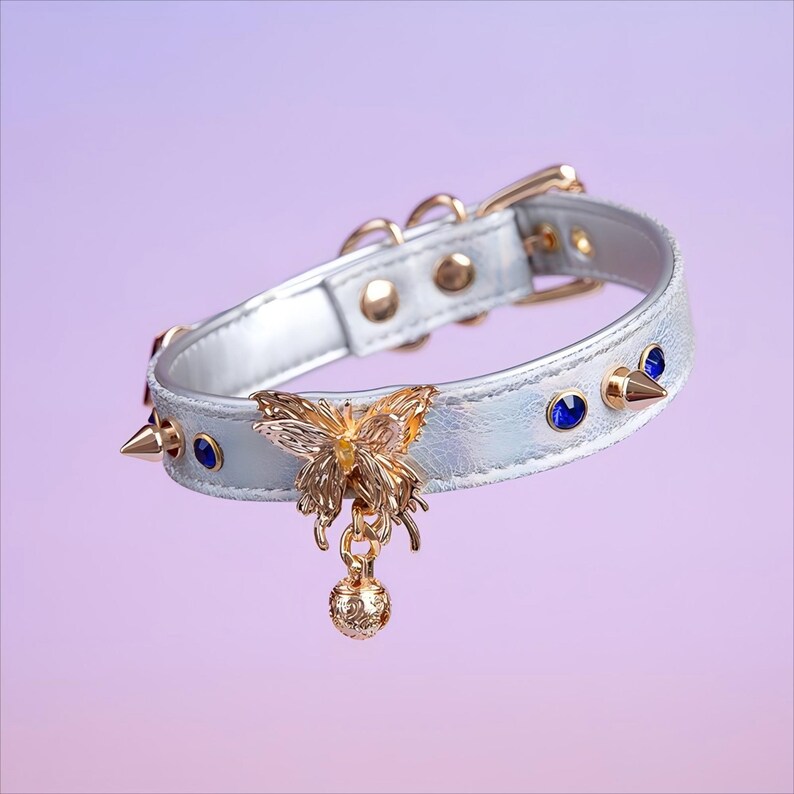 May include: A silver faux leather choker with a gold butterfly charm and blue rhinestones. The choker has gold studs and a bell on the charm.