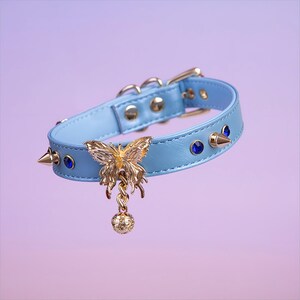 May include: A light blue leather choker with gold spikes and a gold butterfly charm with a dangling ball. The choker has blue rhinestones.
