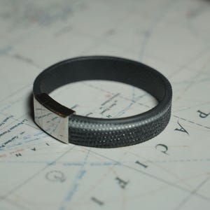 Peut inclure: Un bracelet noir et gris avec un fermoir argenté. Le bracelet est fait d'un matériau texturé et a un léger éclat.