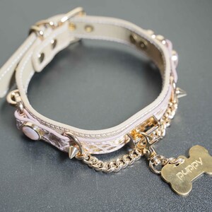 Puede incluir: Un collar de perro rosa y dorado con una cadena y una etiqueta en forma de hueso que dice "Puppy".