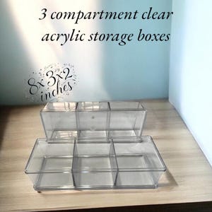 May include: Clear acrylic storage boxes with three compartments. The boxes are 8 x 3 x 2 inches. The text on the image says "3 compartment clear acrylic storage boxes."