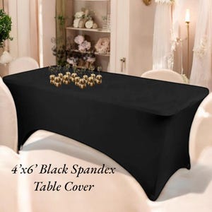 May include: A black spandex table cover, 4 feet by 6 feet, draped over a rectangular table. The cover is smooth and form-fitting. Decorative gold ornaments are placed on the table. The text "4'x6' Black Spandex Table Cover" is visible.