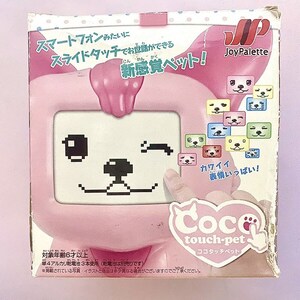 May include: A pink box with a cartoon dog on the front. The box says "Coco touch-pet" and "New Sensation Pet!" in Japanese. The box is for a toy that allows you to interact with a virtual pet.