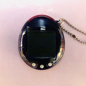 May include: A black and silver digital pet toy with a small screen and three buttons. The toy has a silver chain attached to it.