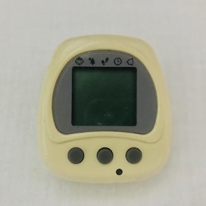 May include: A white plastic digital pet toy with a gray screen and three buttons. The screen displays icons for feeding, playing, and sleeping.