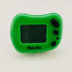 May include: A green plastic handheld digital timer with a black screen and three black buttons. The timer has the word "Hawks" printed on the front.