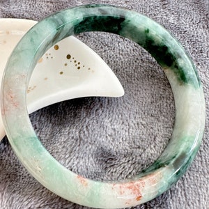 May include: A green jade bangle bracelet with white and pink swirls. The bangle is smooth and polished.