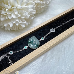 May include: A jade bracelet with a green jade fish charm and silver chain. The bracelet has small green and white stones set in silver.
