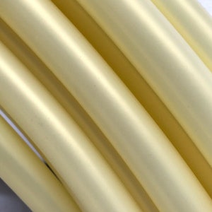 May include: Close-up of several pale yellow, cylindrical objects arranged diagonally. The objects have a smooth, slightly reflective surface, with highlights and shadows creating a sense of depth and texture. The overall composition is simple and abstract.