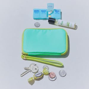 Può includere: Una pochette turchese con cerniera e cinturino da polso verde lime, una chiave, monete, un portapillole e un piccolo flacone di profumo. Il portapillole è etichettato con i giorni della settimana. Sul flacone di profumo c'è la scritta "Duo Plus".