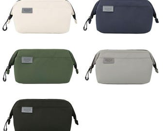 May include: Five rectangular cosmetic bags in various colors: off-white, navy blue, olive green, light gray, and black. Each bag has a small rectangular label and a black zipper pull. The bags are designed for travel and personal care.