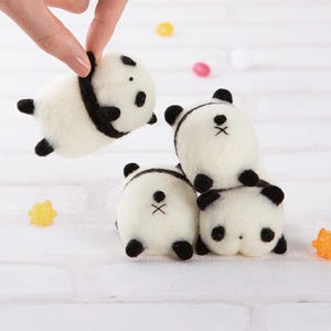 May include: Four small, white, felt panda bears with black eyes, noses, and ears. The pandas are arranged in a stack, with the top panda facing the viewer and the other three facing away.