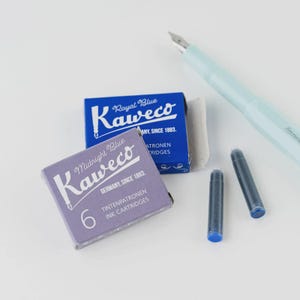 Puede incluir: Una pluma estilogr&aacute;fica Kaweco azul claro con plum&iacute;n plateado, dos cartuchos de tinta y dos cajas de cartuchos de tinta Kaweco. Una caja es azul y dice "Royal Blue", la otra es morada y dice "Midnight Blue".