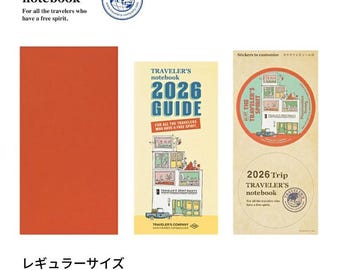 May include: An orange Traveler's notebook refill, a 2026 Guide, and a sticker sheet. The notebook and guide feature the text "TRAVELER'S notebook" and "For all the travelers who have a free spirit." The sticker sheet is round and says "2026 Trip TRAVELER'S notebook."