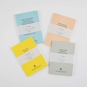 Puede incluir: Cuatro cuadernos en colores pastel: azul, melocotón, amarillo y verde. Cada cuaderno tiene una banda blanca con texto. El cuaderno azul dice: "Los ojos de las personas son fascinantes". El cuaderno amarillo dice: "Lo que dijiste, ahora mismo".