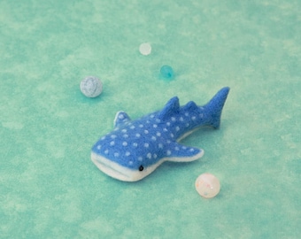 May include: A blue felt whale shark with white spots. The whale shark is lying on a light blue surface.