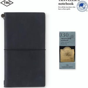 May include: A dark blue Traveler's notebook with a matching elastic closure. A brass clip is displayed next to the notebook. The packaging reads "TRAVELER'S notebook" and "Brass Clip".