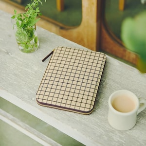 以下が含まれることがあります： ベージュと黒のチェック柄のジッパー付きケース。茶色のジッパープルとトリムが付いています。ケースの隣には、薄茶色の液体が入った小さな白いマグカップがあります。緑のハーブが入った水のグラスも画像にあります。