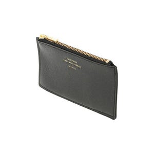 May include: A black wallet with a gold zipper and the text "Quitterie C'est Mon Trésor" in gold lettering. The wallet is rectangular and appears to be made of a textured material.