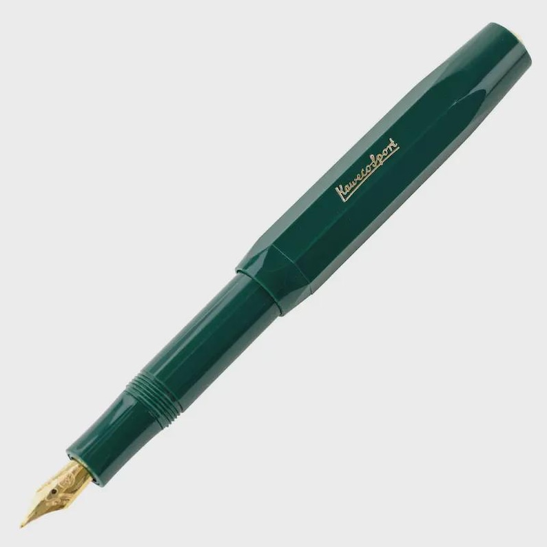 Puede incluir: Una pluma estilogr&aacute;fica verde oscuro con un plum&iacute;n dorado. El bol&iacute;grafo tiene un cuerpo facetado y el texto "Kaweco Sport" est&aacute; impreso en el lateral. El bol&iacute;grafo est&aacute; en &aacute;ngulo diagonal sobre un fondo blanco.