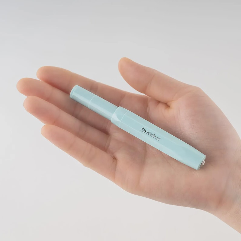 Puede incluir: Una pluma estilogr&aacute;fica Kaweco Sport azul claro. El bol&iacute;grafo se sostiene en una mano y tiene el logotipo de Kaweco Sport impreso en el lateral. El bol&iacute;grafo tiene un cuerpo hexagonal y una tapa redondeada.