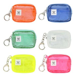 May include: Six small, rectangular, transparent pouches in various colors: orange, blue, green, white, yellow, and pink. Each pouch has a silver-colored keychain and a small white label with black text that reads "UTILITY MINI DELFONICS."