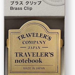 May include: A brass clip for a Traveler's notebook, presented in a box. The clip features the text "TRAVELER'S COMPANY JAPAN" and "TRAVELER'S notebook". The box has the number "030" and the words "TRAVELER'S notebook" and "Brass Clip".