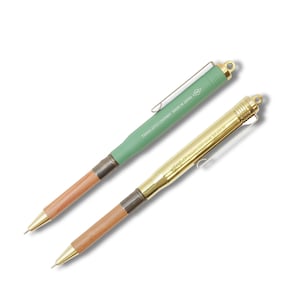 May include: Two mechanical pencils with wood and metal barrels. One pencil is green with a brass clip and the text "TRAVELER'S COMPANY MADE IN JAPAN". The other pencil is gold with a brass clip and the text "TRAVELER'S COMPANY MADE IN JAPAN".