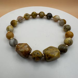 Op de afbeelding: Een bruine en gele agaat armband met gouden accenten. De armband heeft verschillende ronde en gefacetteerde kralen.